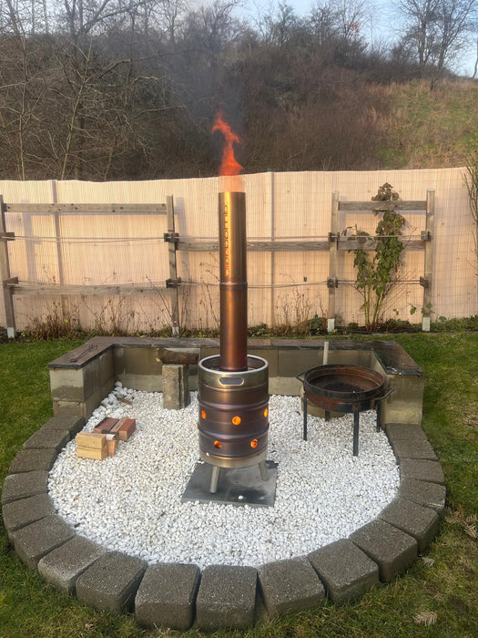 bierbomb® in der Dämmerung, daneben Brennholz und eine Feuerschale