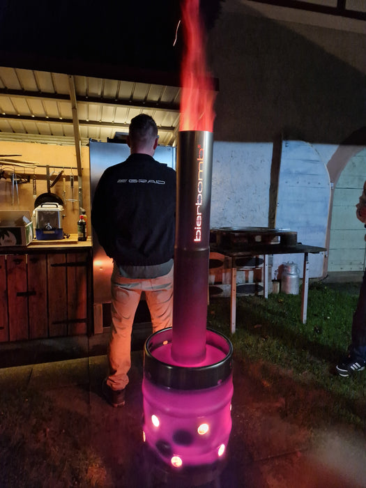 bierbomb® bei Nacht unter einem Vordach, das Rohr glüht rot, eine Person steht daneben
